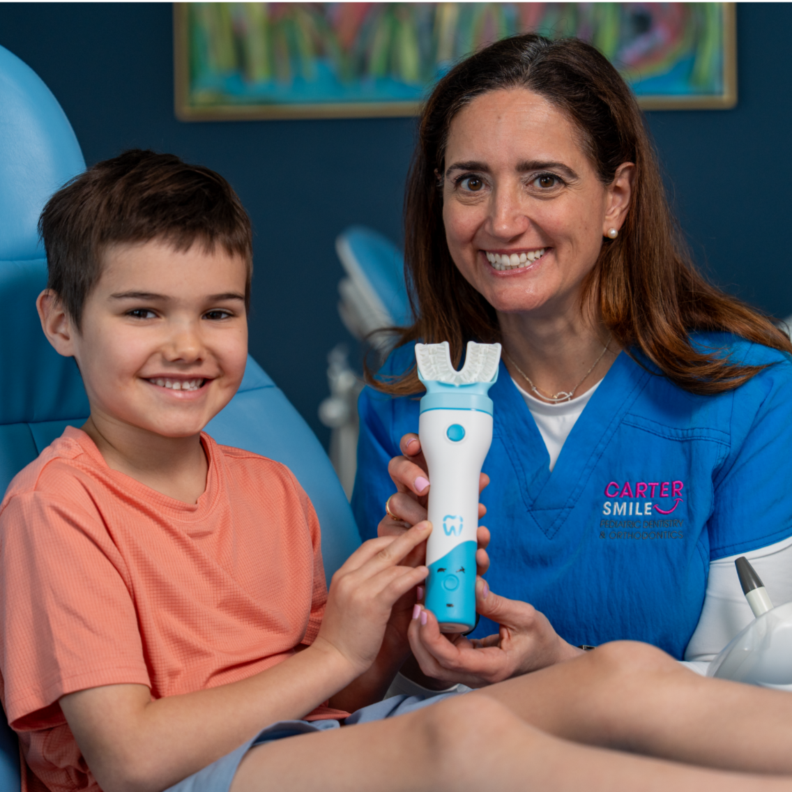 Dental professional holding a device with a child in a dental chair, smiling.