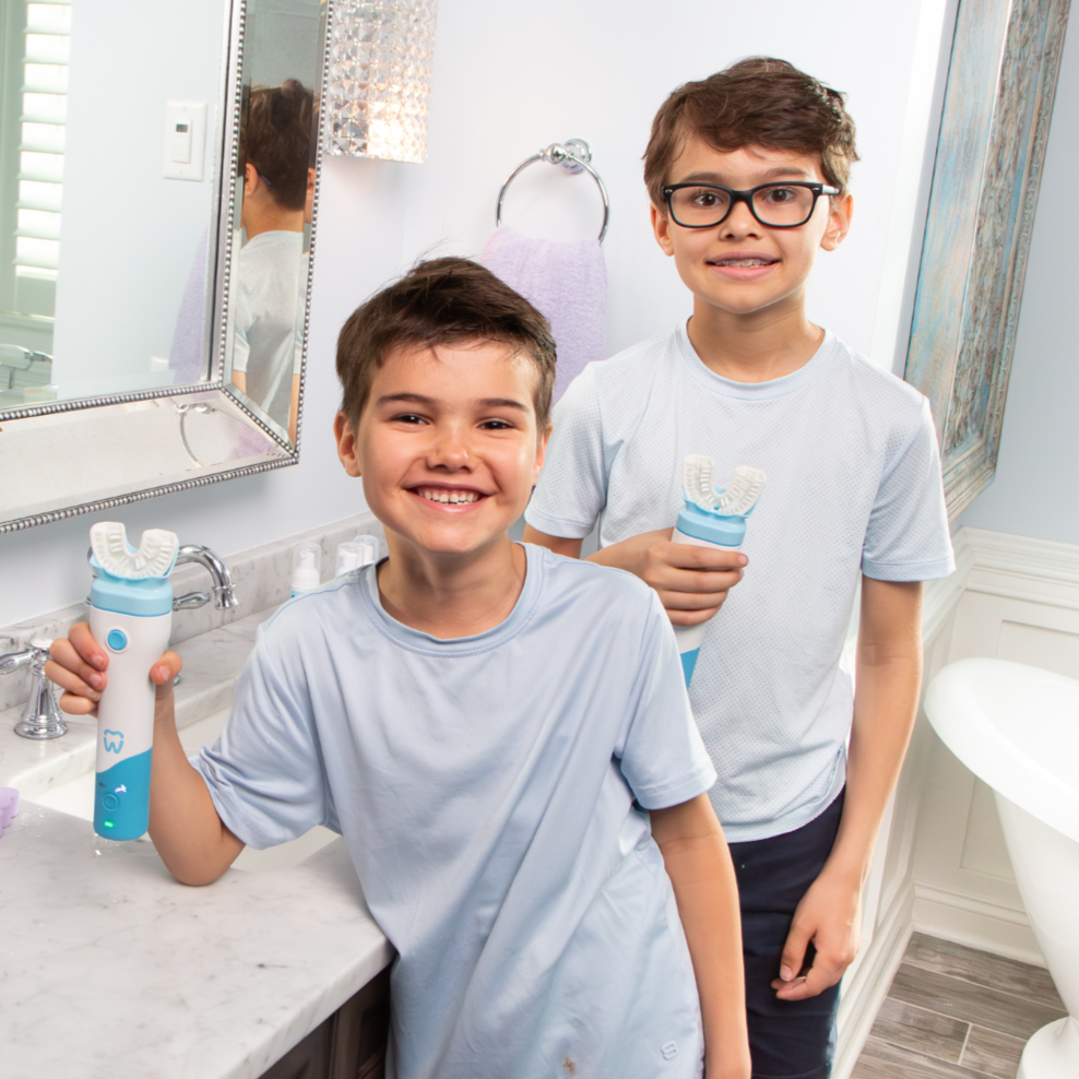 Two boys in a bathroom holding bottles, with a sink and mirror in the background.