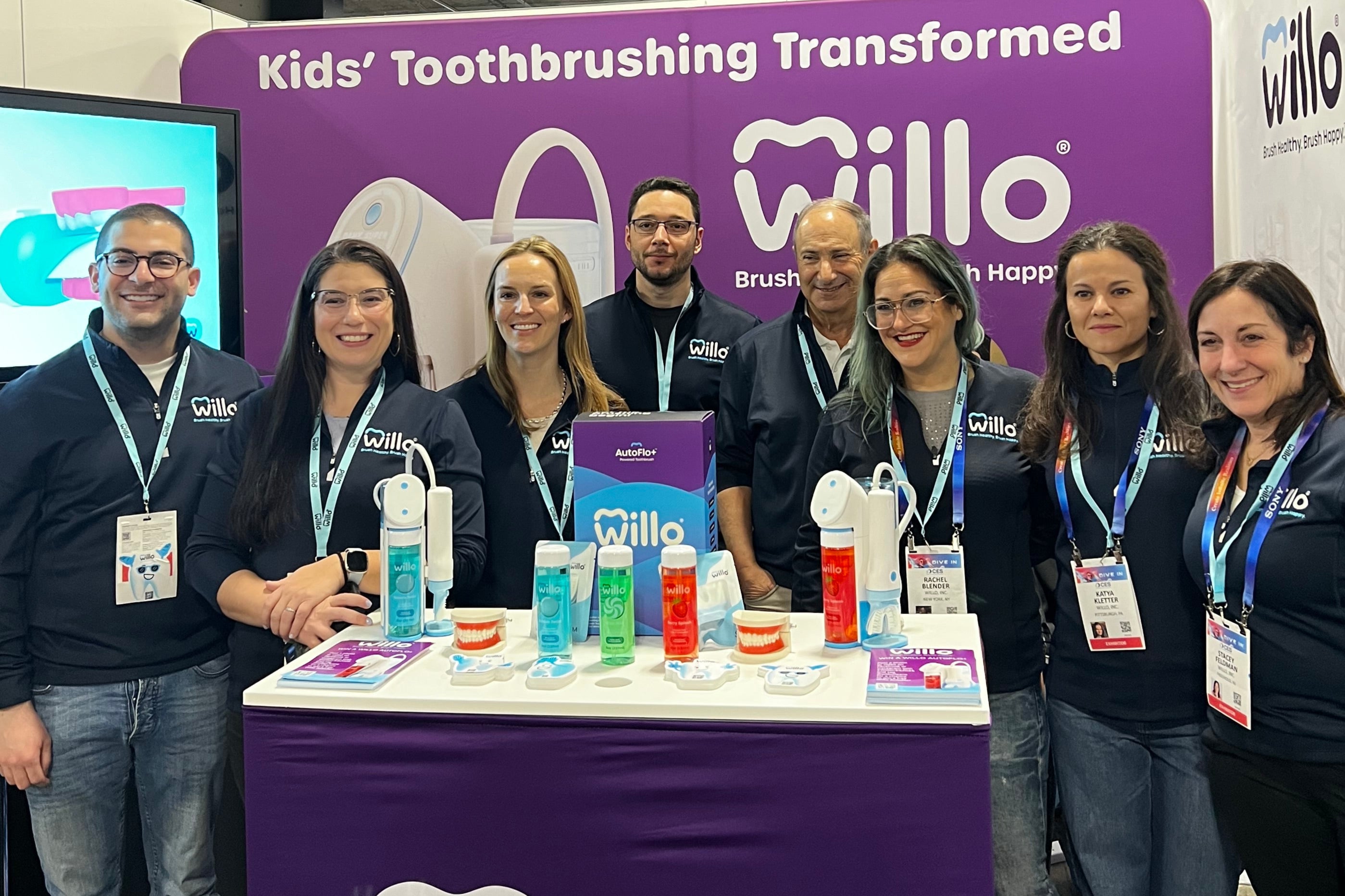 Group of people posing in front of a Willo branded booth at an event.