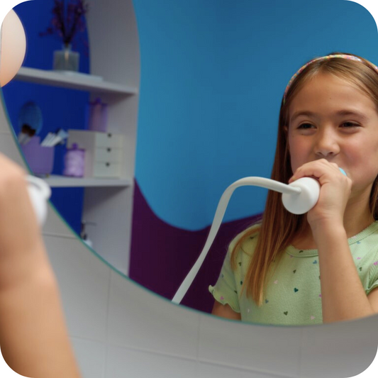 Girl wearing a green shirt brushing her teeth with Willo kids automatic brushing toothbrush in a bright bathroom