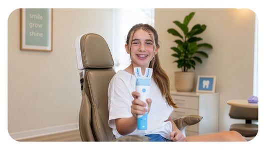 A smiling young teenage girl with braces sits in an orthodontic treatment chair holding out a white and blue Willo automated oral care device with a U-shaped brush head.