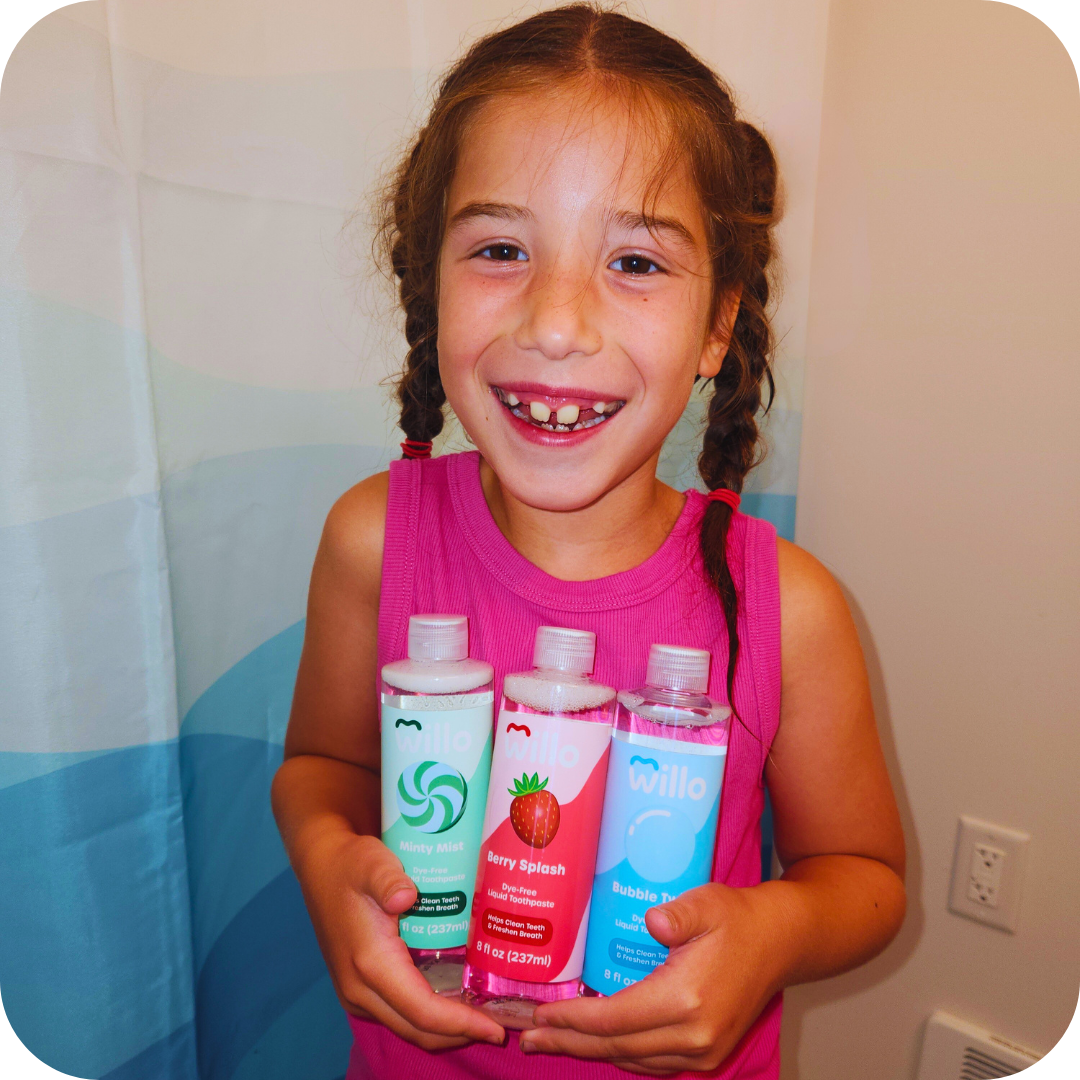 Girl in bathroom holding 3 bottles of dye free kids toothpsate