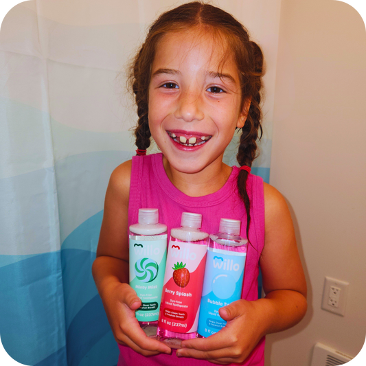 Girl in bathroom holding 3 bottles of dye free kids toothpsate