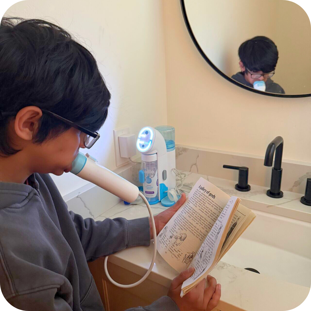 Boy with autism reading a book while using Willo kids automatic brushing toothbrush in a bathroom