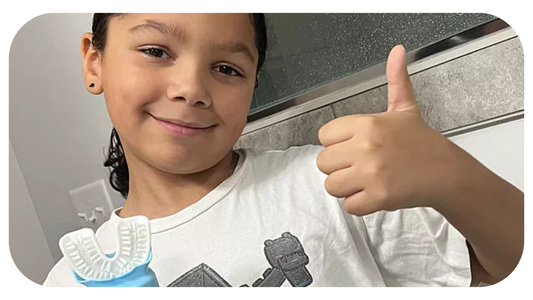 boy giving thumbs up and smiling with his willo auto brushing kids toothbrush in gray bathroom