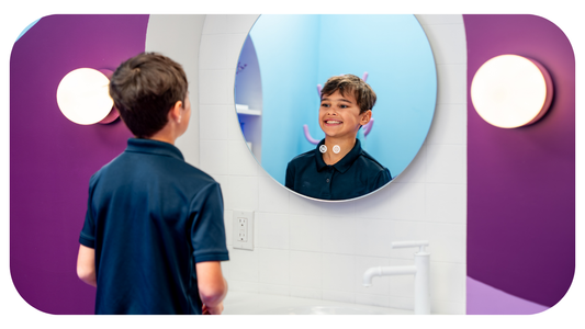 boy in navy shirt smiling into a mirror in a purple bathroom