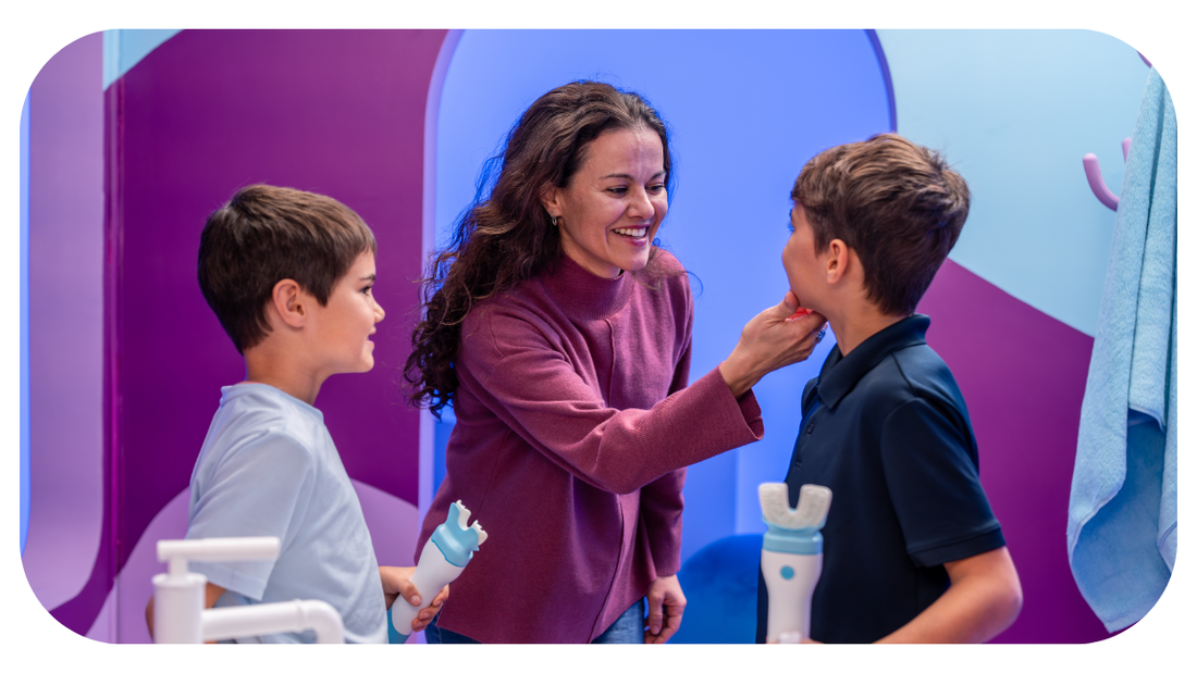 mom inspecting teeth of two sons in colorful bathroom