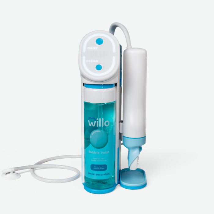 A studio product shot of the white and blue Willo automated smart toothbrush base station against a plain white background. The docking unit features an illuminated circular control ring with 