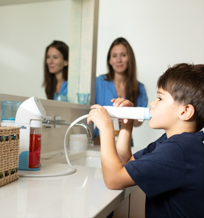 Child using an automatic toothbrush with a woman watching in a bathroom setting