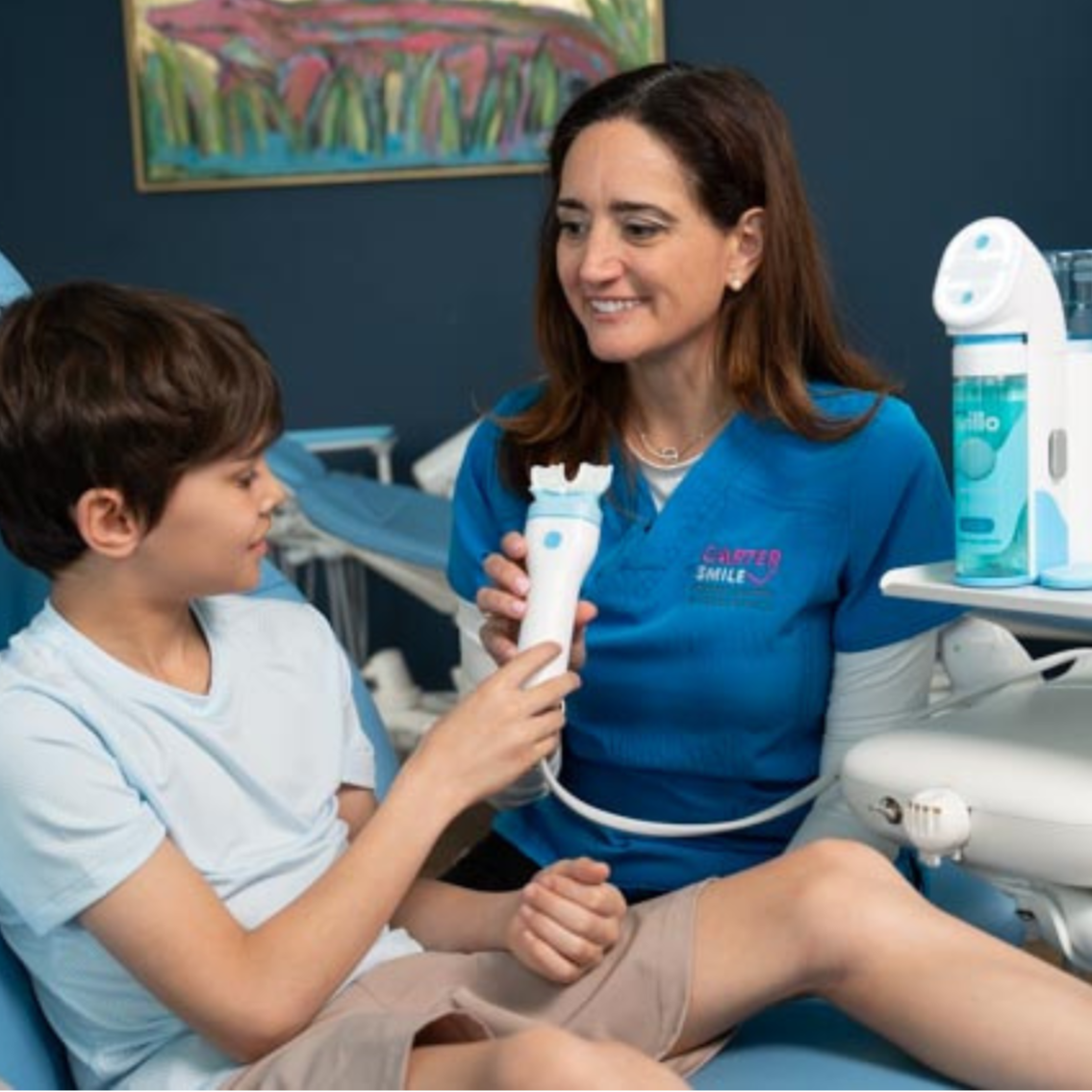 Woman in dental uniform assisting a child with dental care equipment in a dental office.