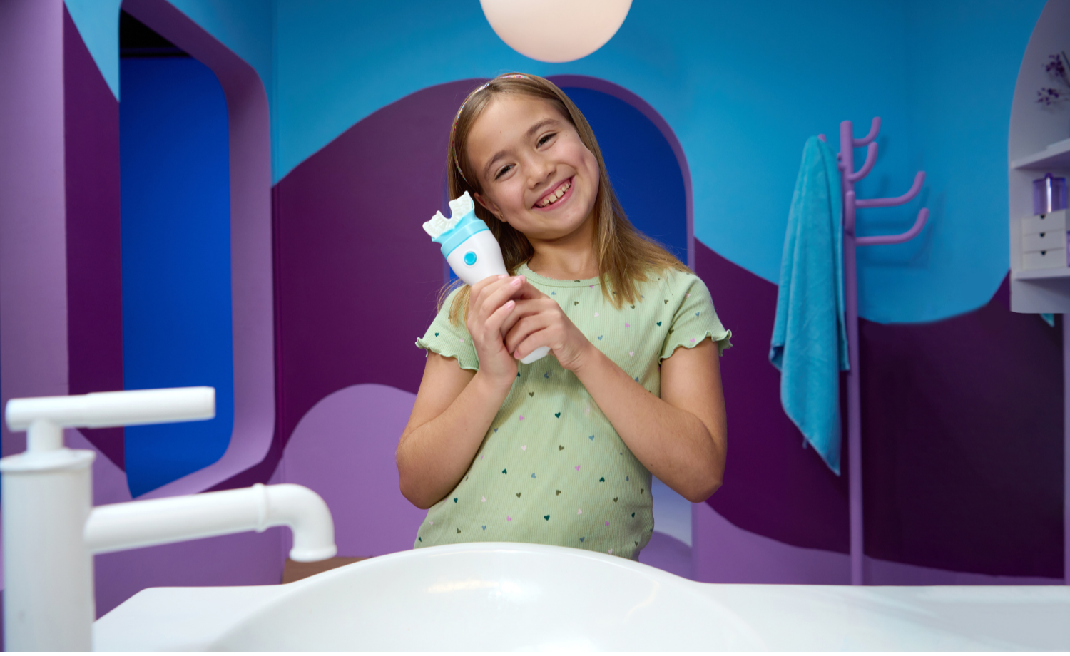 Young girl holding a bottle in a colorful room with purple walls and a white bed.