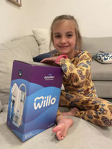 Real customer lifestyle photo of a young girl sitting with the Willo AutoFlo+ powered toothbrush product packaging on a couch at home.